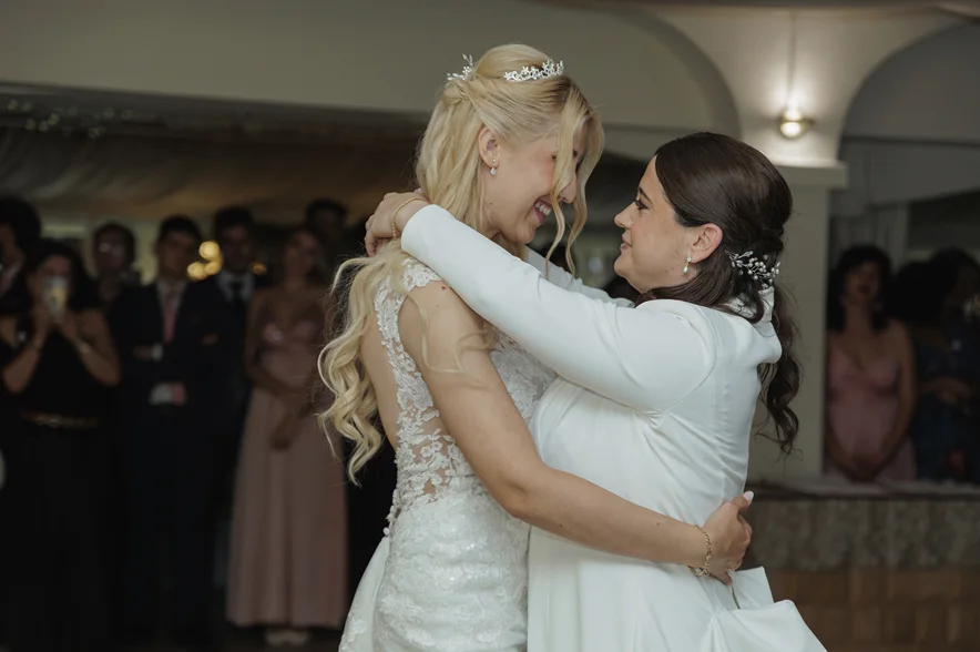 Dos novias se abrazan y se ríen en mitad del salón, rodeadas de invitados.